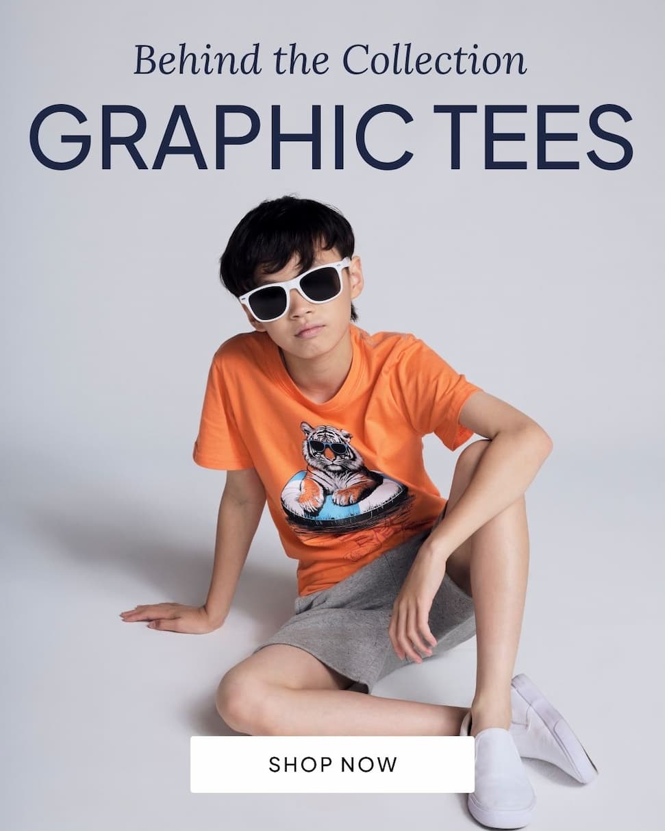 boy wearing orange graphic tee on grey background with text behind the collection graphic tees and shop now button