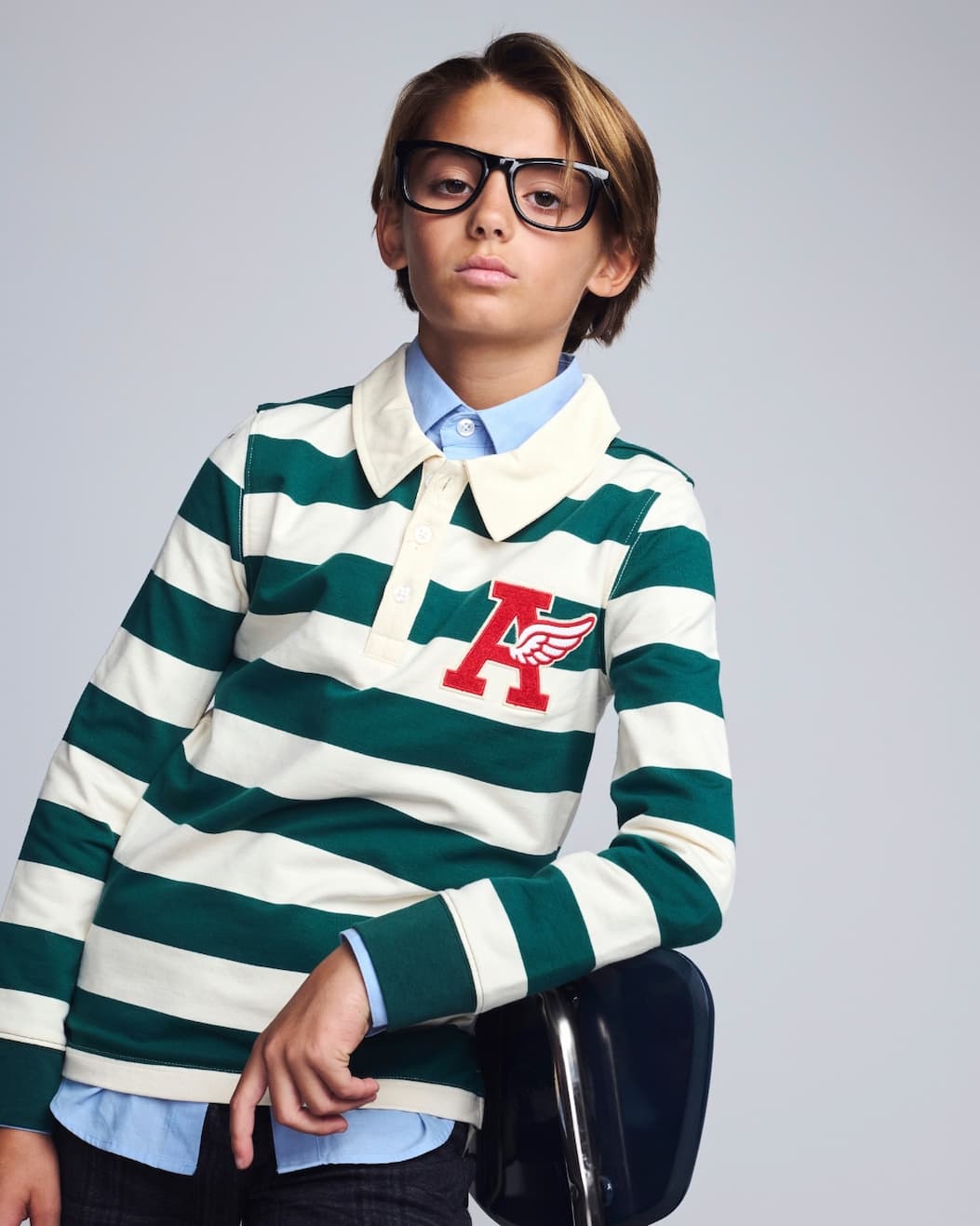 Boy on grey background wearing green and white striped polo