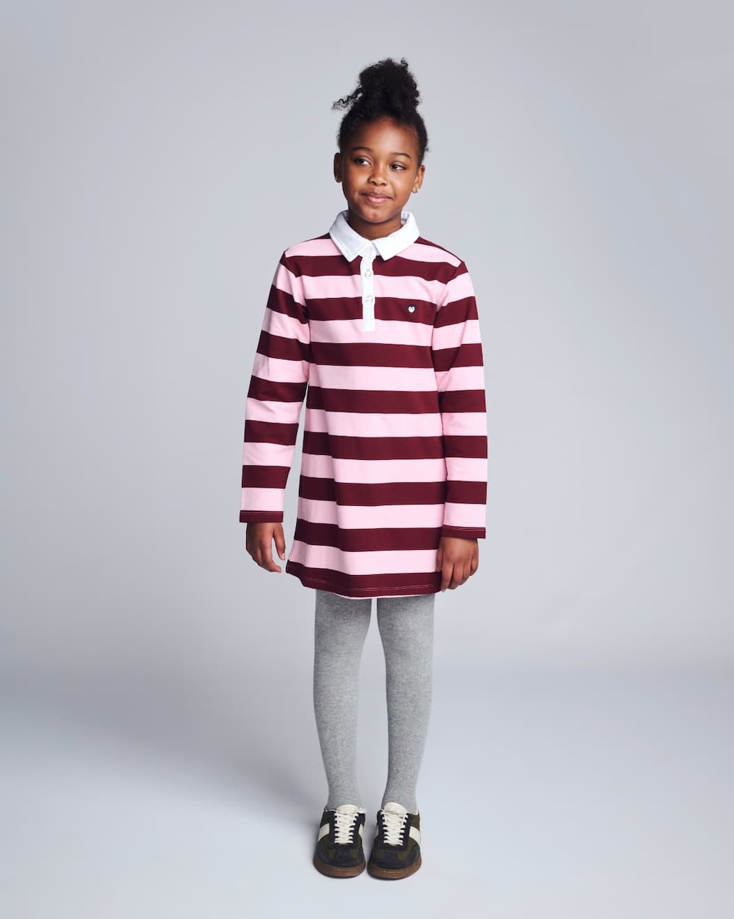 Girl on grey background wearing pink striped long sleeve polo dress 
