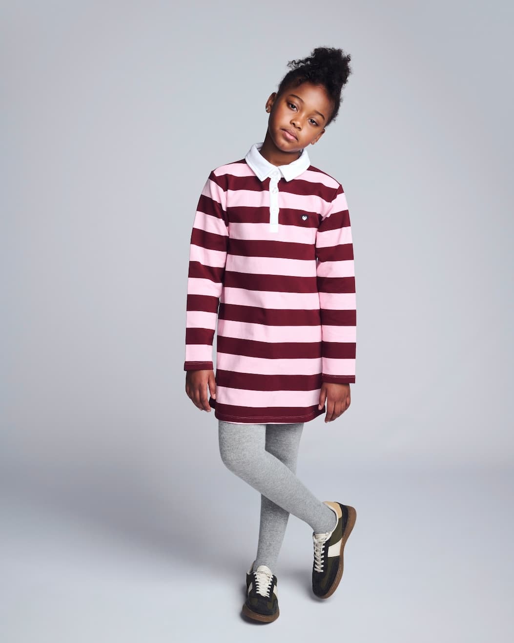Girl on grey background wearing pink striped long sleeve polo dress 