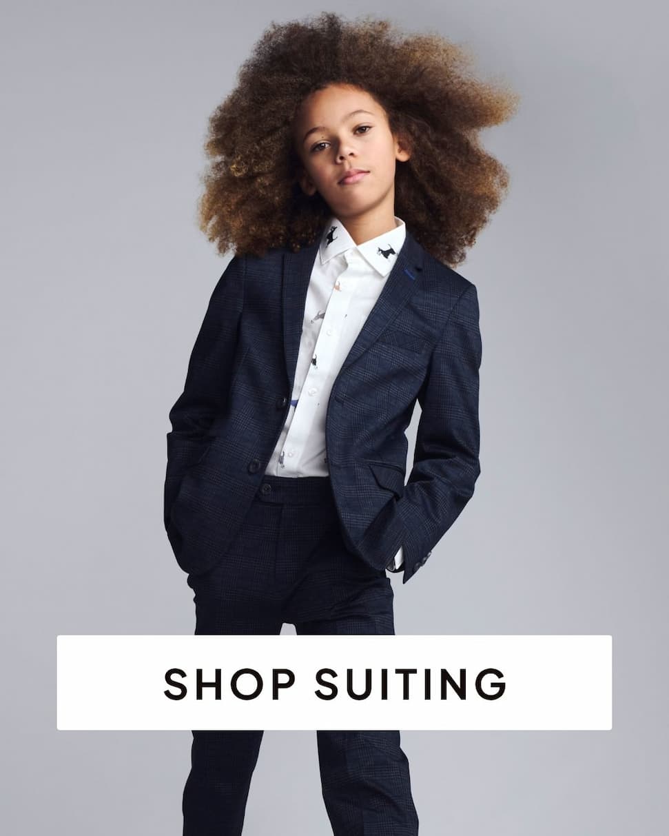boy wearing navy suit and white printed dress shirt on grey background with text shop suiting