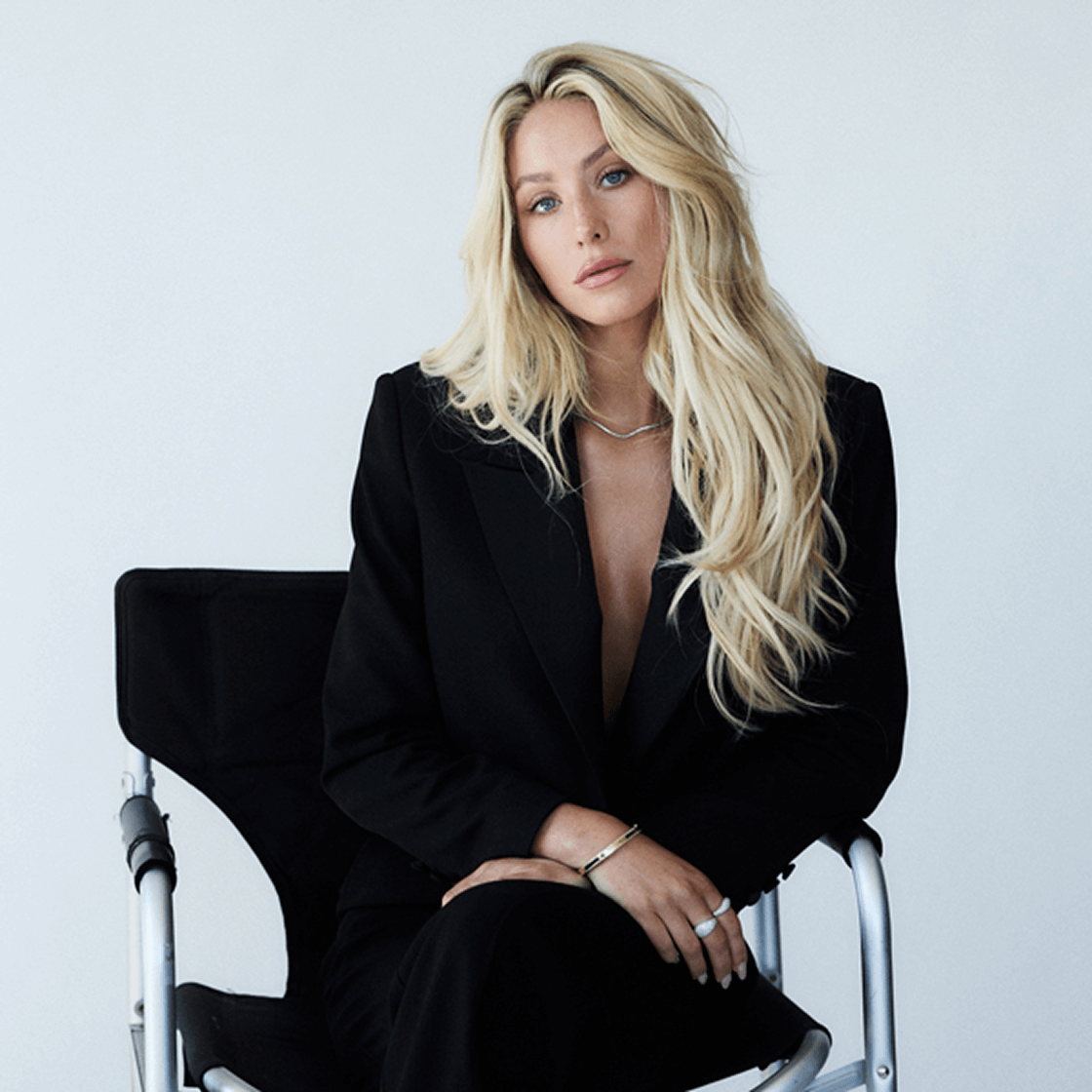 Woman with blonde hair wearing black suit sitting in a black chair.