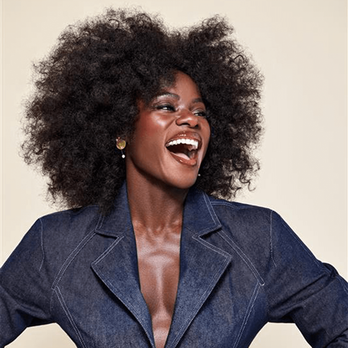 Smiling woman with black hair wearing denim suit standing.