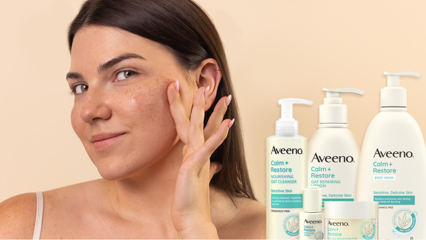 Image of a woman applying Aveeno Calm and Resore Oat Gel Moisturizer to her cheek, along with all the Aveeno Calm and Restore products lined up.
