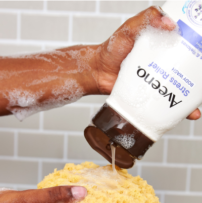 Image of woman applying the Aveeno Stress Relief Body Wash onto a bath sponge.