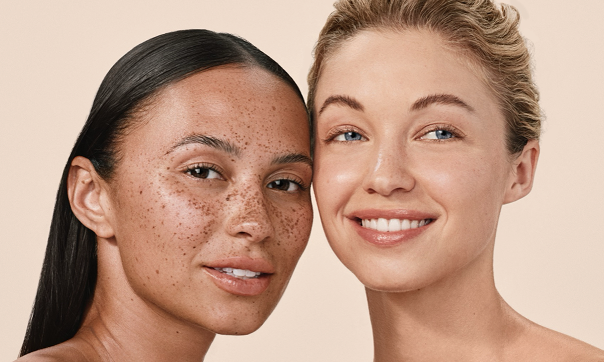 Close up of two women’s faces as they are slightly smiling, and showing clear, glowing skin.