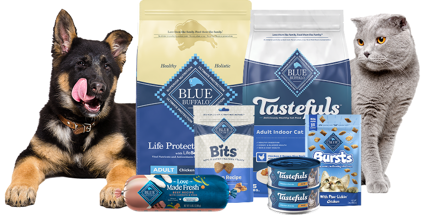 A German Shepherd puppy licking its mouth and a gray cat are next to various bags, rolls, and cans of BLUE pet food and treats.