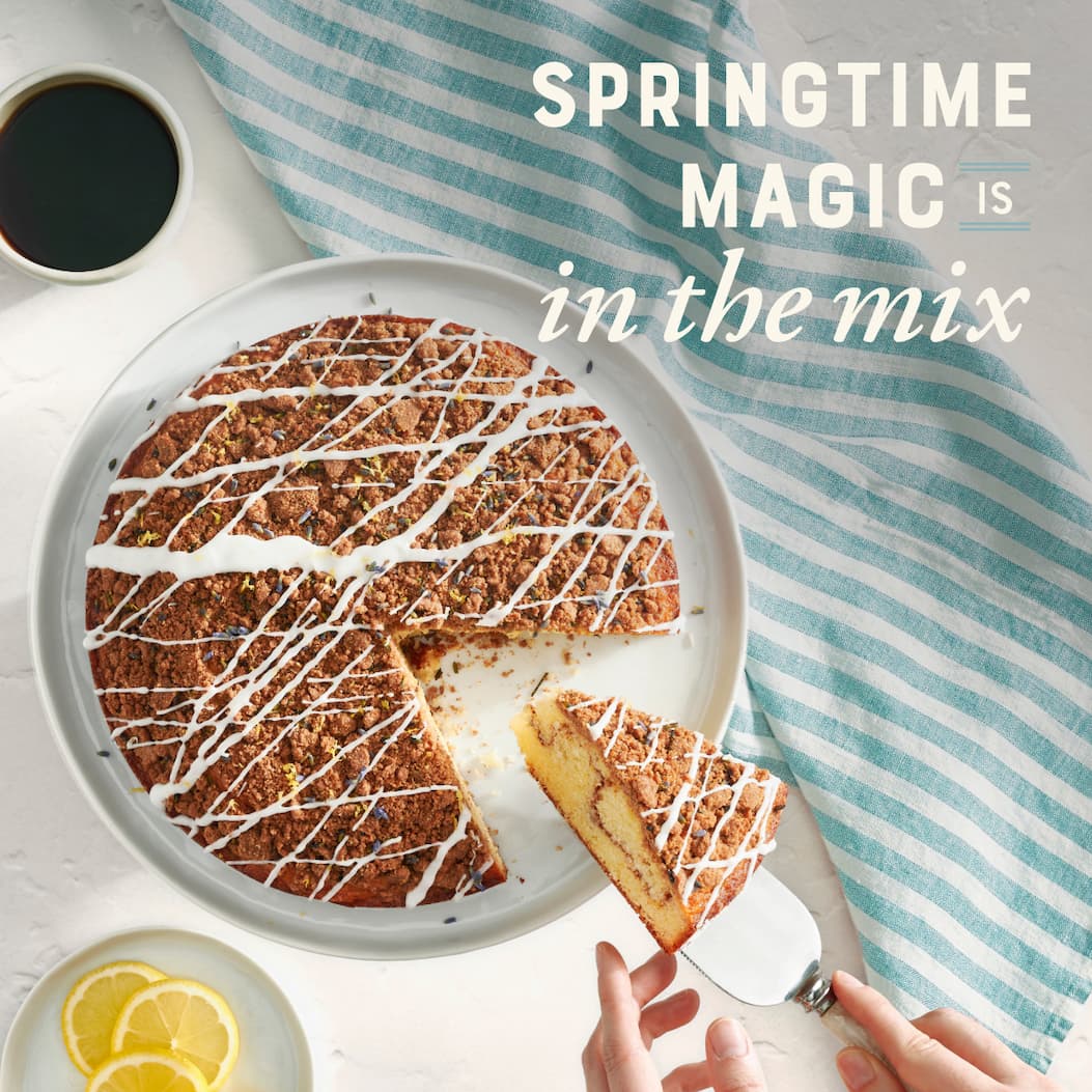 Springtime magic is in the mix. Image of Cinnamon Swirl Coffee Cake with a set of hands removing a slice.