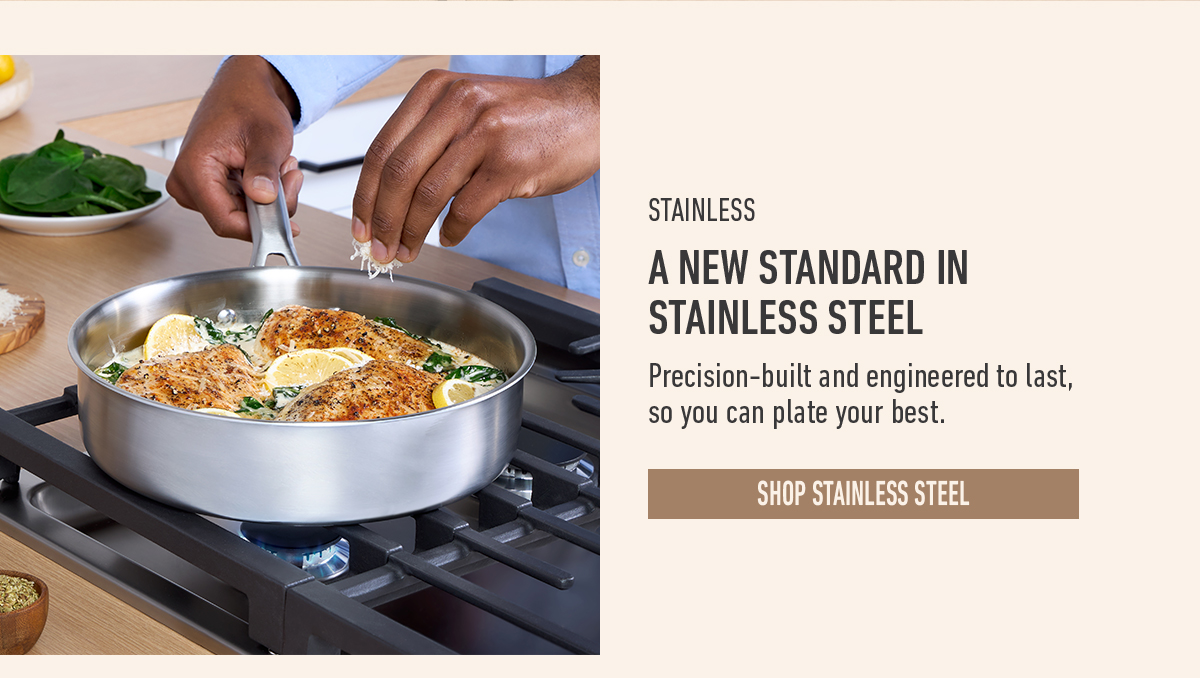 A person seasoning cooked salmon and spinach in a stainless steel pan on a stove, text reads a new standard in stainless steel, button shop stainless steel