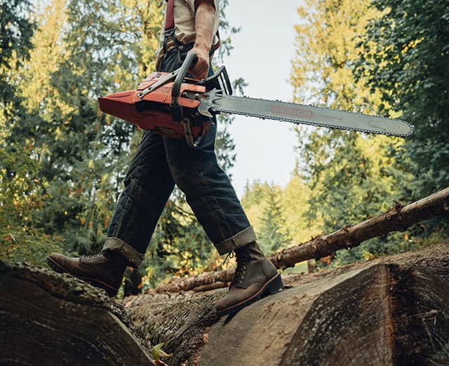 A man wearing Chippewa Loggers while holding a chainsaw.