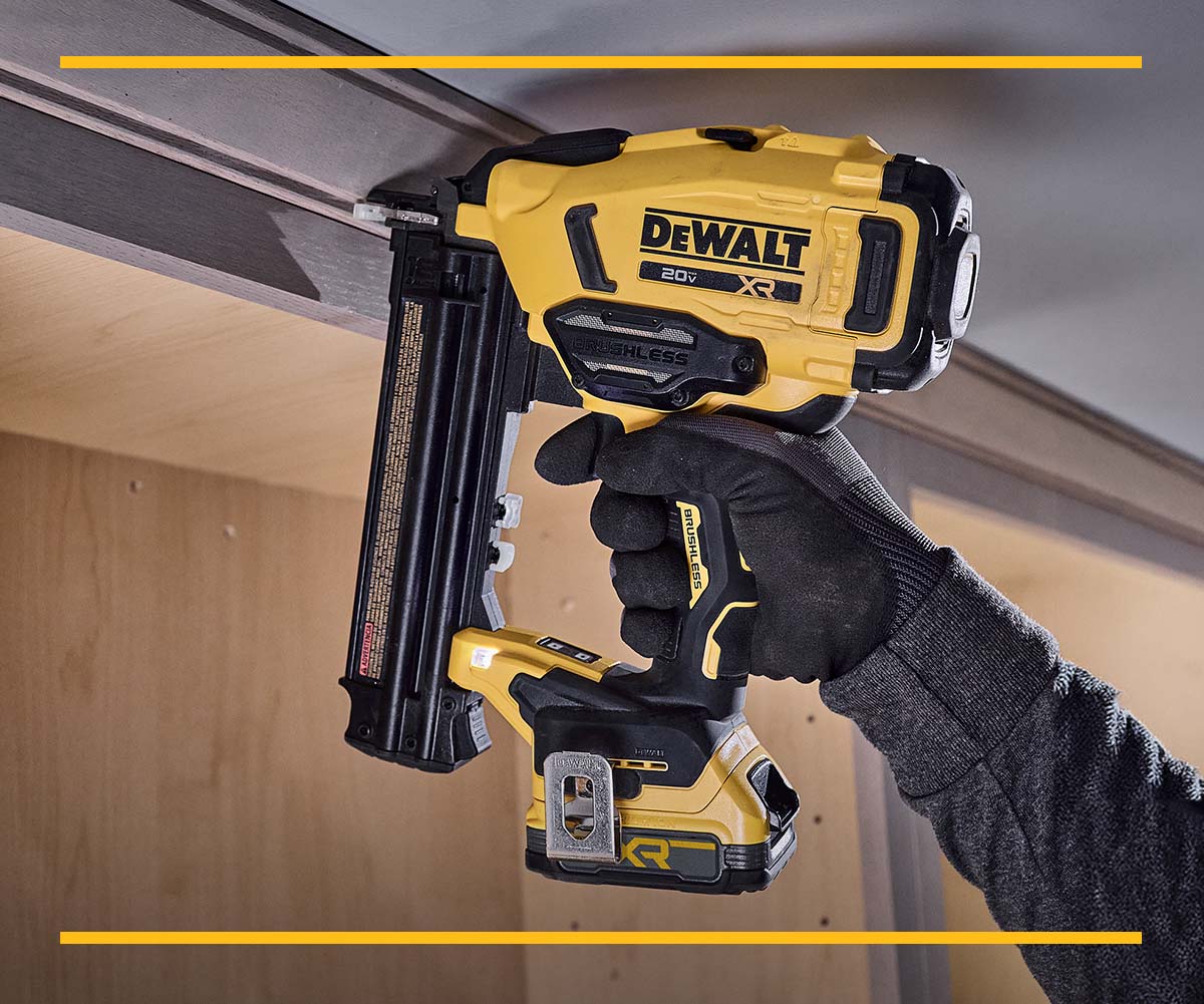 A person uses a DEWALT DCN210 20V cordless nailer to attach trim to cabinets. The tool is yellow and black, and the user is wearing gloves and safety glasses.