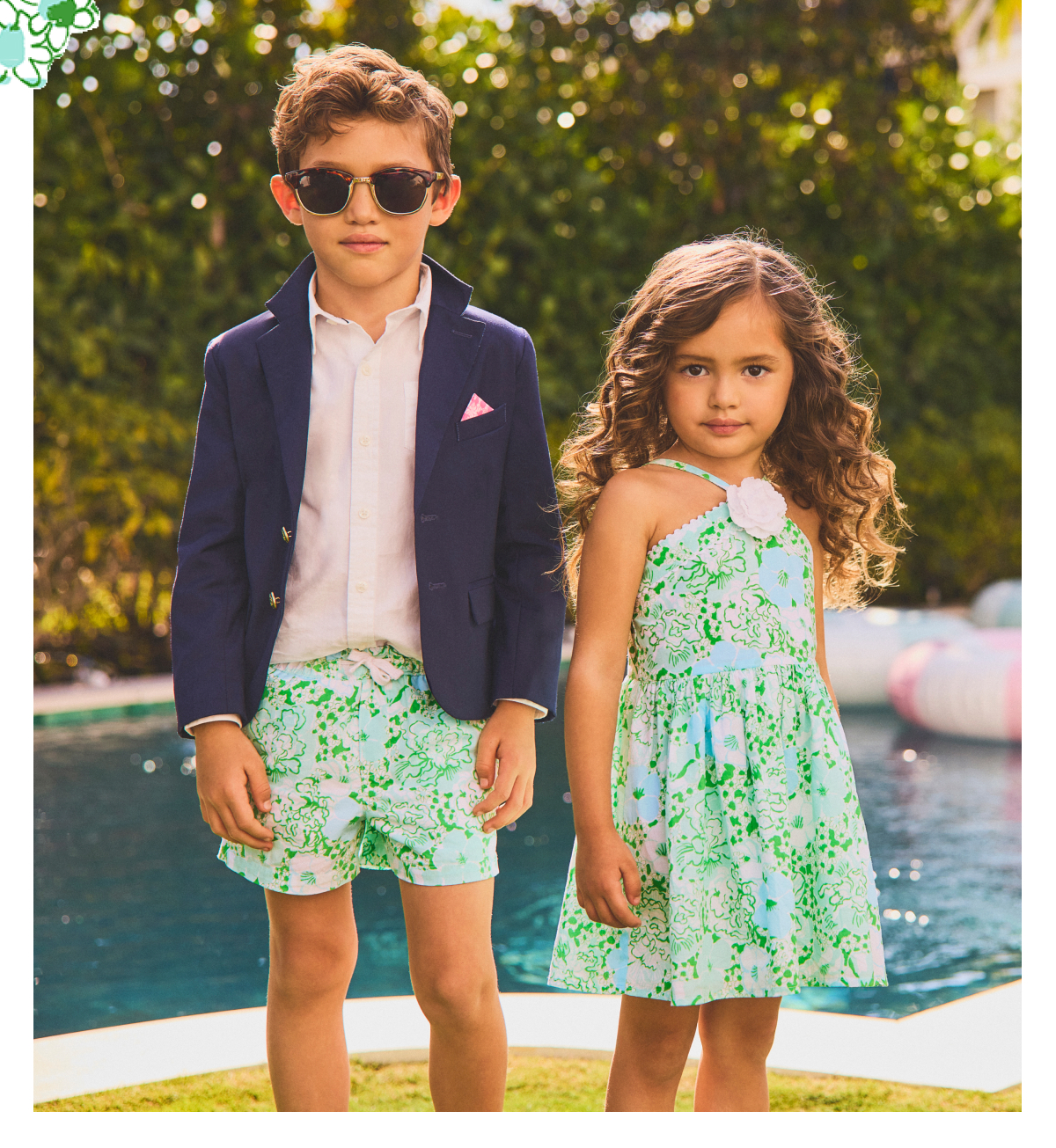 Children wearing matching green and white floral print outfits standing by a pool