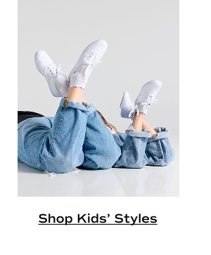 A woman and a child laying next to one another on their stomachs with their feet in the air, ankles crossed. They are both wearing cuffed wide-leg jeans paired with the Keds Champion Canvas Lace-Ups in white and frilly white ankle socks. Shop Kids’ Styles.