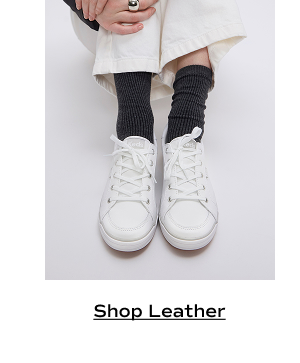 A pair of Center III Leather Lace-Ups in white shown on foot paired with dark grey socks and cream pants. Shop leather.