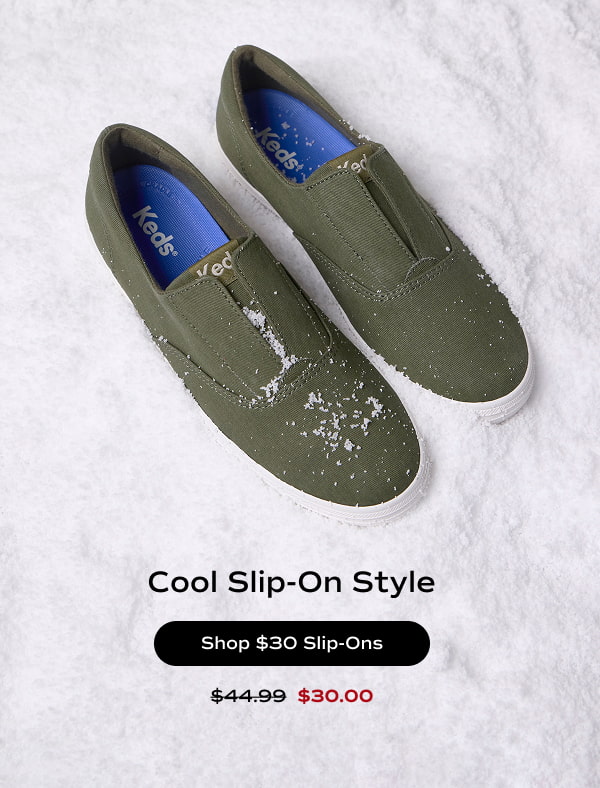 A pair of Keds Champion Twill Round Toe Slip-Ons in olive green which were $44.99 and are now $30.00 for a limited time. The sneakers are sitting in sparkling snow with text underneath that says Cool Slip-On Style. Shop $30 Slip-Ons.