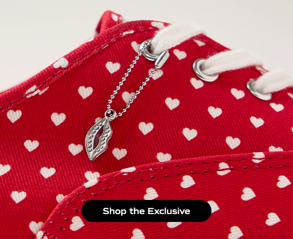 A closeup of the Keds Champion Canvas Lace-Up in an exclusive Valentine’s Day print of repeating little white hearts against a bright red background. The image is animated showing the silver lips shoelace charm swinging back and forth. Shop the Exclusive.
