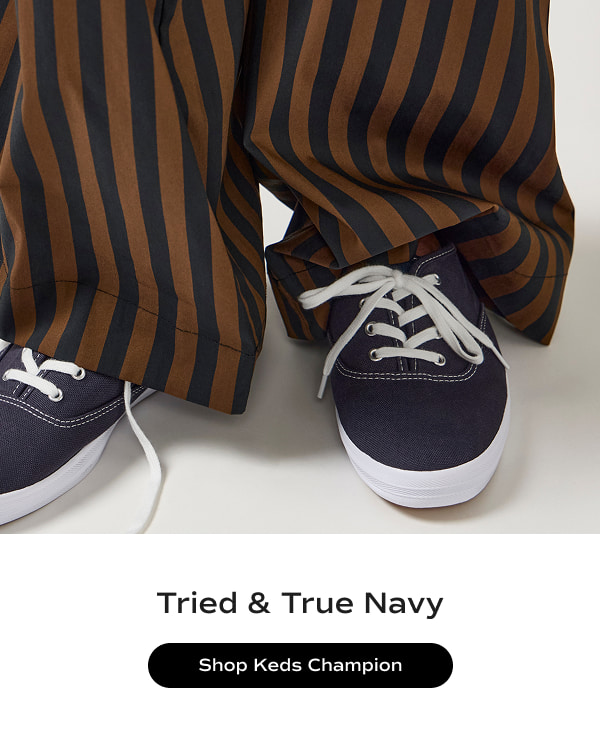 The Keds Champion Originals Lace-Up in navy paired with brown-and-blue striped wide-leg pants. The text says Tried & True Navy. Shop the Keds Champion.