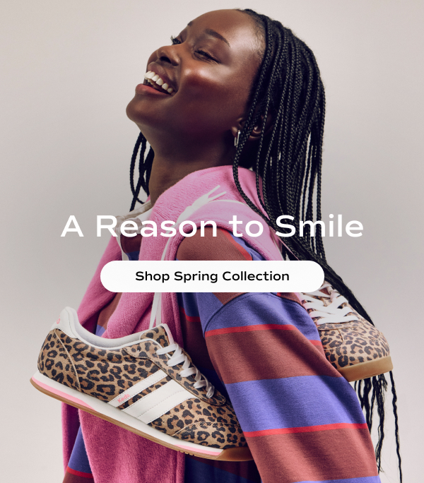 A smiling woman is wearing a long-sleeve, blue-and-red rugby shirt with a pink sweater around her shoulders and carrying the new Revival Leo Suede Lace-Up in tan/brown. The text says A Reason To Smile. Shop the Spring Collection.