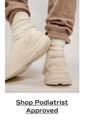 A closeup of a pair of BlissMove Knit Slip-Ons in snow white/parchment shown on foot paired with brown knit joggers and scrunched cream socks. Shop Podiatrist Approved.
