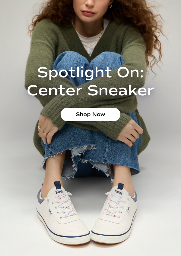 A woman sitting, holding her knees. She is wearing a green V-neck sweater, raw-edge jeans, and the Center III Leather Nautical Slip-On in snow white/navy. The email says Spotlight On: Center Sneaker. Shop Now.
