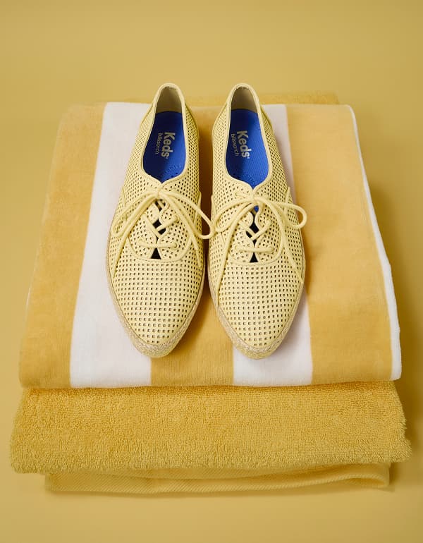 Top‑down view of the Keds Champion Point Low Wave Perf Leather Lace‑Ups in yellow placed on folded yellow-and-white striped towels.