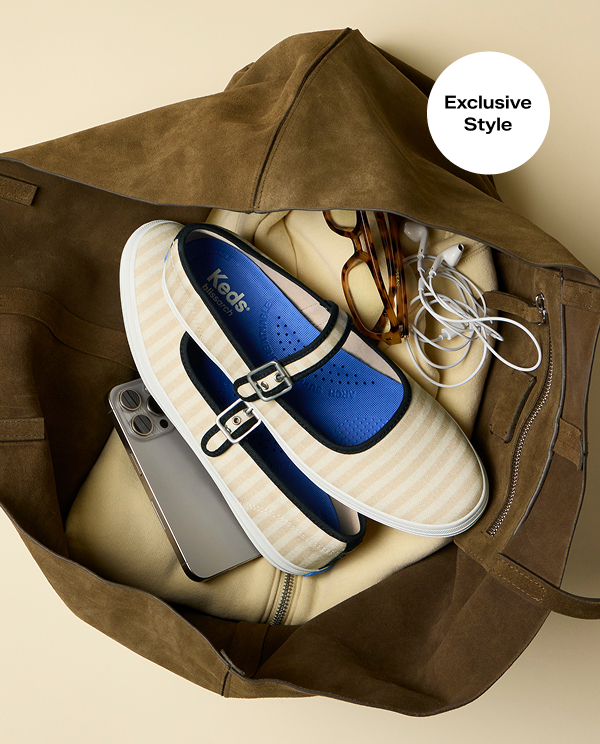 A top-down view of a pair of Maisie Printed Stripe Twill Mary Janes sitting in a large brown suede tote bag along with a yellow zip-up sweatshirt, glasses, earphones, and a smartphone. A callout on the image notes that this style is a Keds.com exclusive.