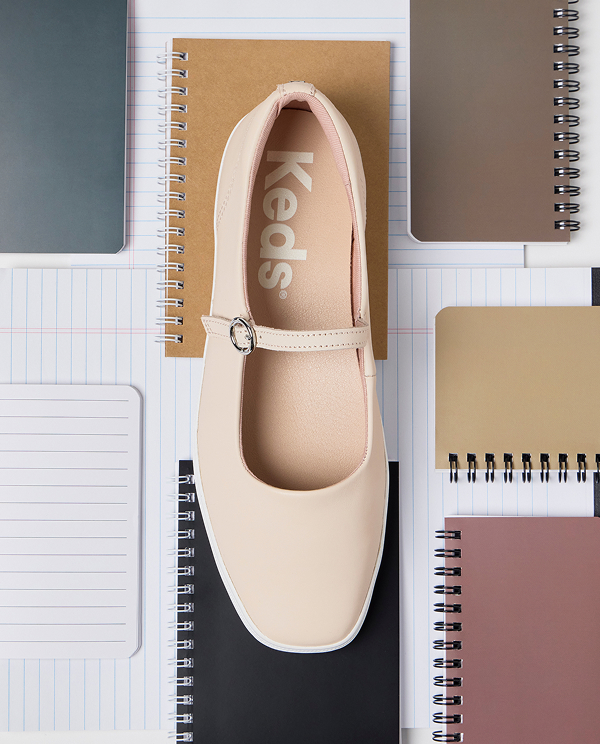 A top-down view of the Square Toe Mary Jane Leather flat in peony pink sitting on top of a desk with a number of spiral notebooks and lined paper.