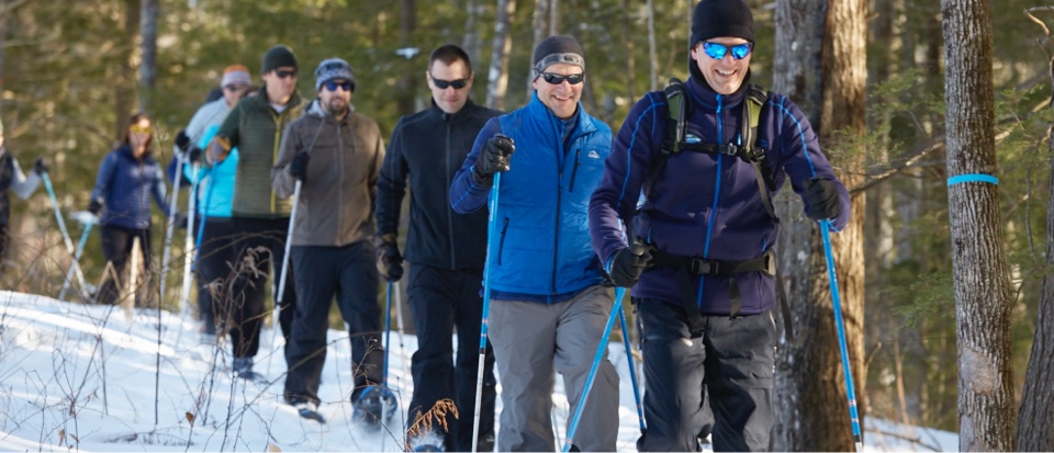 Group of people snowshoeing through the woods.
