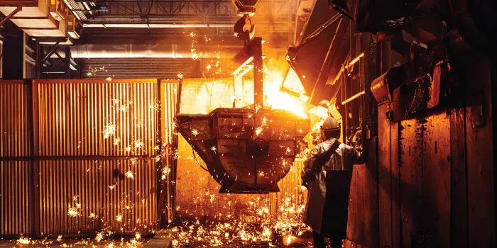 Worker oversees molten metal pouring in a foundry with sparks flying.