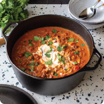 Cast iron Dutch oven filled with tomato stew topped with sour cream and cilantro