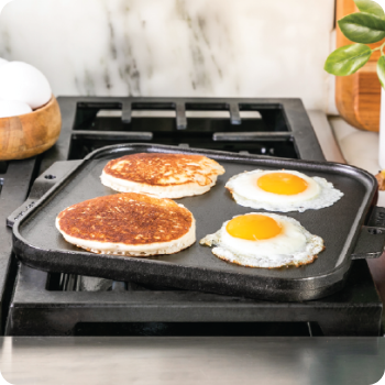 Cast iron griddle with pancakes and sunny-side-up eggs on a stovetop