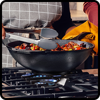  Cast iron wok with vegetables being tossed over a gas flame