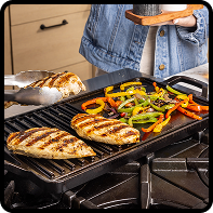 Cast iron grill pan with chicken and vegetables cooking on a stovetop