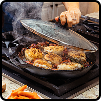 Cast iron skillet with chicken being cooked, lid lifted to release steam
