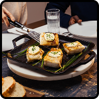 Square cast iron griddle with fish fillets topped with melted butter and herbs
