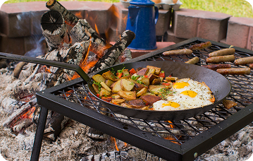 Fried eggs and potatoes being prepared in a carbon steel skillet over a campfire