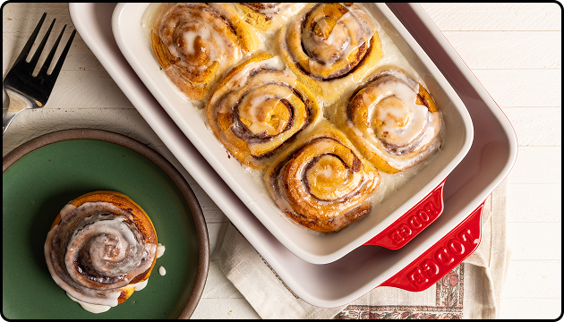 Iced cinnamon roles in a red stoneware casserole dish