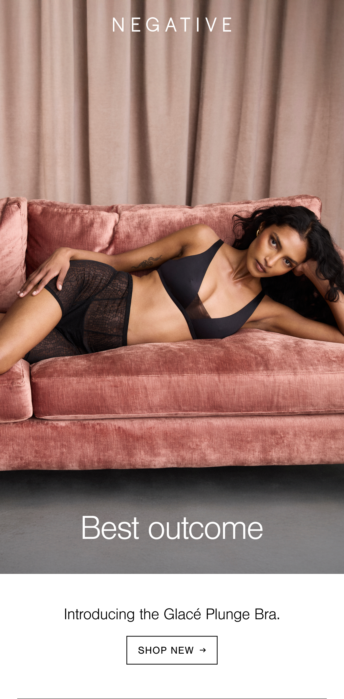 Model is laying on a sofa wearing our new Glacé Plunge Bra in Black. The bra has soft structure, a high gloss sheen, and a sheer tulle center for extra support. The bra is paired with our Serpente Boxer in Black: a high-rise and stretchy-sheer boxer made from our playful snakeskin lace. 