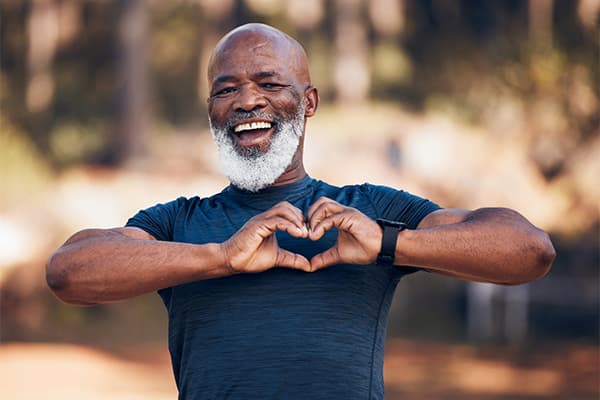 dark skinned man with white beard smiling and making a heart shape with his hands