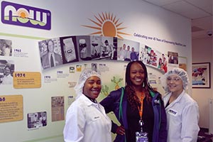 Three NOW Employees standing in front of a NOW history wall