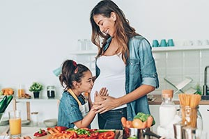Pregnant mom in the kitchen with her daughter who is kissing her pregnant belly