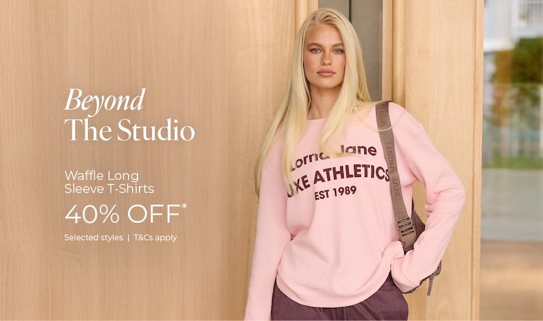 Model wearing pink Lorna Jane Waffle Long Sleeve T-Shirt, 40% off*, leaning against timber wall.
