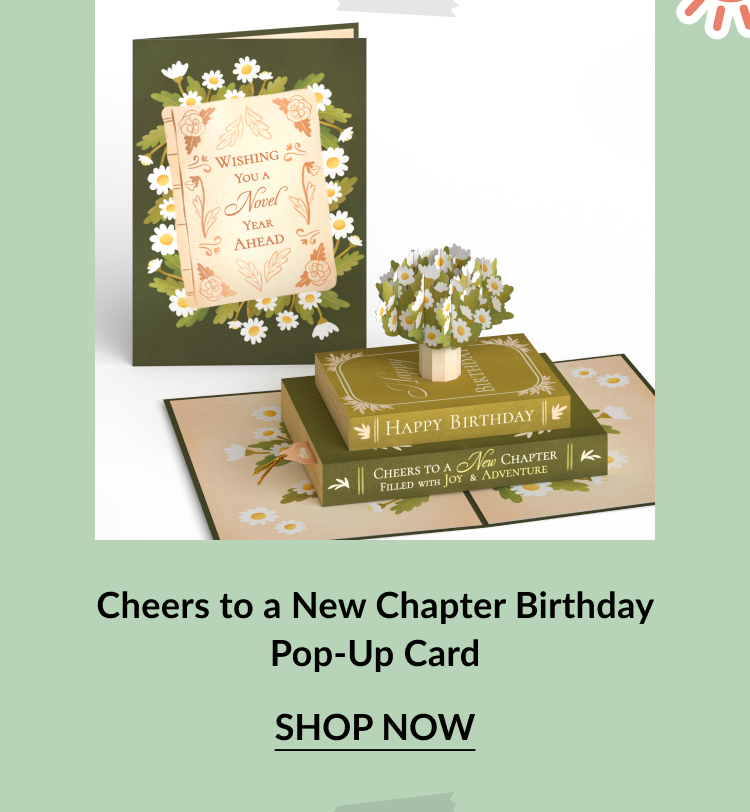 Birthday card styled like a stack of books with floral details and the message Wishing You a Novel Year Ahead on the cover. Inside reveals a pop-up tree growing from stacked books labeled Happy Birthday and Cheers to a New Chapter. Call-to-action below reads Cheers to a New Chapter Birthday Pop-Up Card – Shop Now.