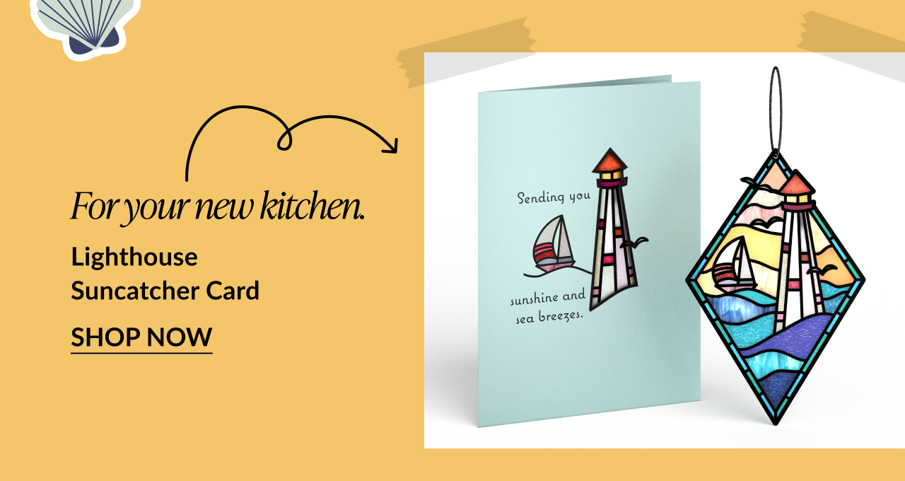Card featuring a red-and-white lighthouse and sailboat, next to a lighthouse-themed diamond-shaped suncatcher. Card reads: 'Sending you sunshine and sea breezes.' Text below says: 'For your new kitchen. Lighthouse Suncatcher Card.' Button reads 'Shop Now.