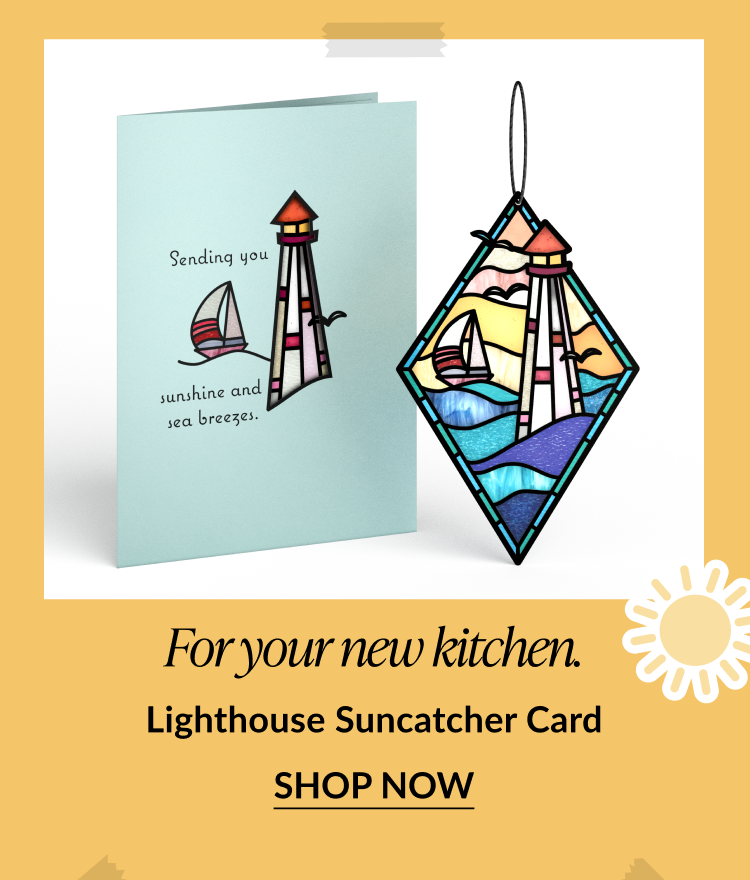 Card featuring a red-and-white lighthouse and sailboat, next to a lighthouse-themed diamond-shaped suncatcher. Card reads: 'Sending you sunshine and sea breezes.' Text below says: 'For your new kitchen. Lighthouse Suncatcher Card.' Button reads 'Shop Now.