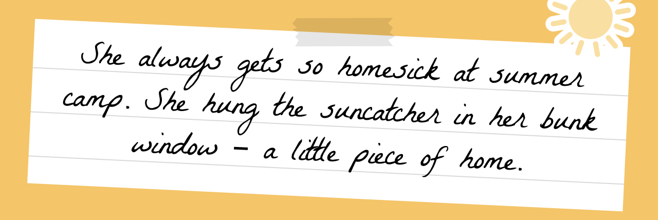 Handwritten note on lined paper with tape and a beach shell sticker, reading: 'She always gets so homesick at summer camp. She hung the suncatcher in her bunk window – a little piece of home.