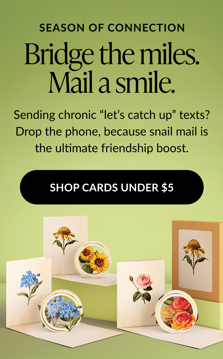 Promotional banner with floral-themed pop-up cards and boxed sets arranged on green platforms. Text encourages sending cards to reconnect with friends. Black CTA button reads ''SHOP CARDS UNDER $5.''