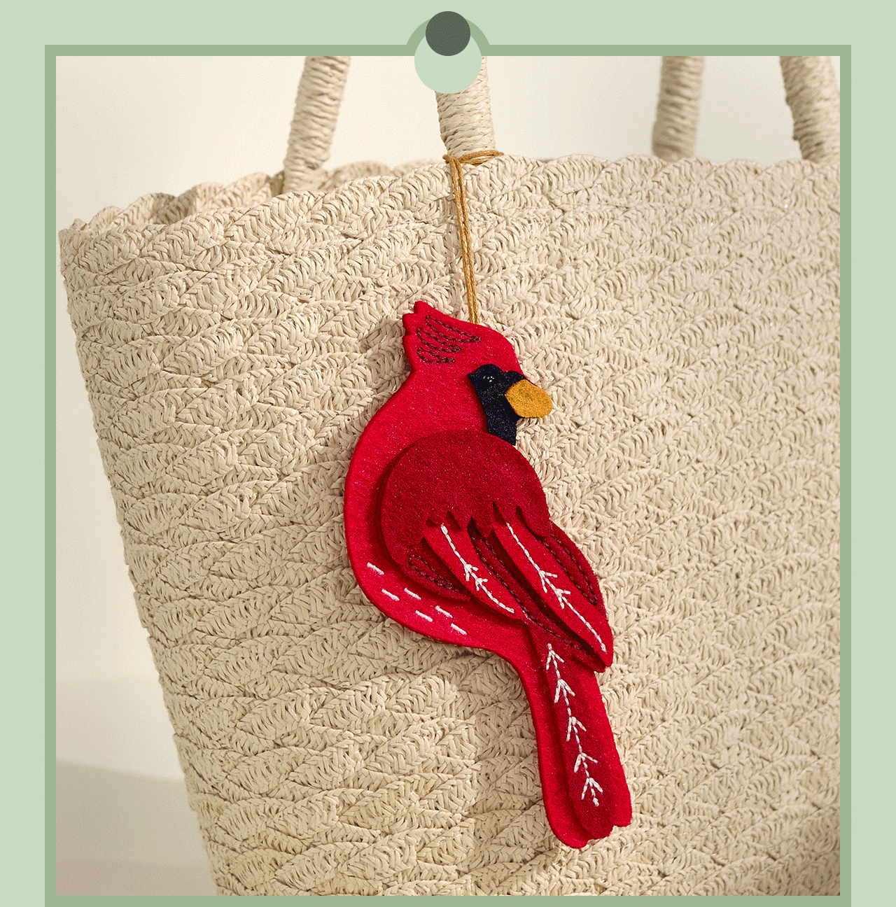GIF of a red cardinal charm attached to a woven beige tote bag.