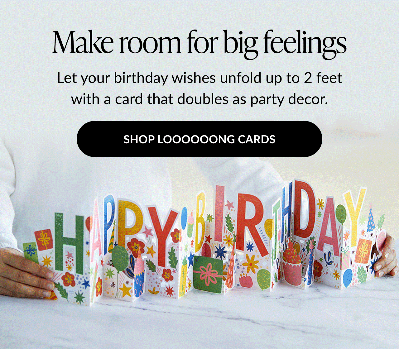 Animated image of a person holding a colorful, extra-long pop-up birthday card that spells out HAPPY BIRTHDAY with the text Make room for big feelings and SHOP LOOOOOONG CARDS