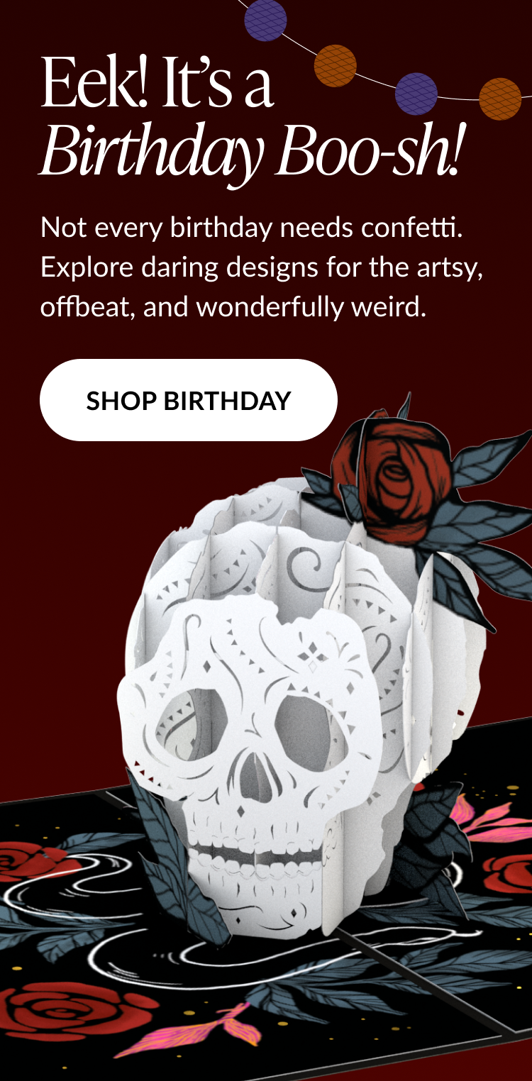 Pop-up birthday card shaped like a white sugar skull with a red rose, set against a dark red background with string lights